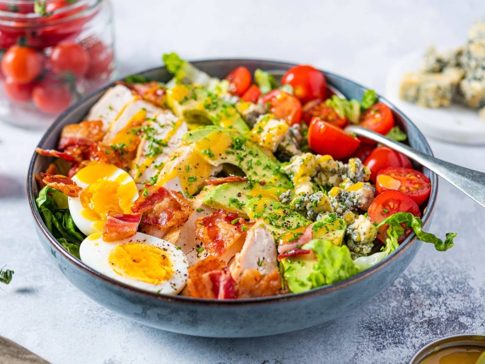 En frisk Cobb-salat med egg, kylling, avokado, tomater og blåmuggost i en skål.