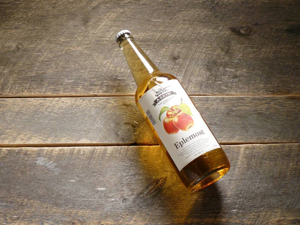 En glassflaske med eplesaft eller eplejuice ligger på et trebord, med etikett som viser et eplebilde.