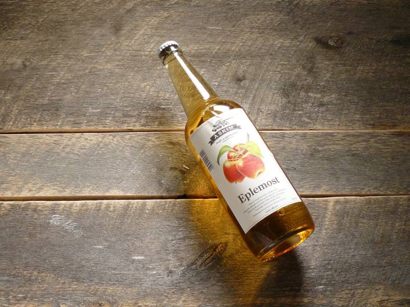 En glassflaske med eplesaft eller eplejuice ligger på et trebord, med etikett som viser et eplebilde.
