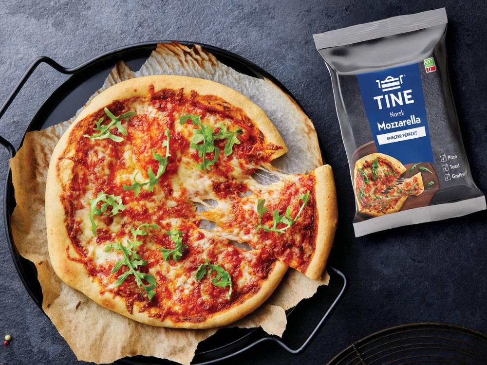 En ferdig pizza med ost og tomatsaus på en svart plate, med en pakke TINE® Mozzarella ved siden av.