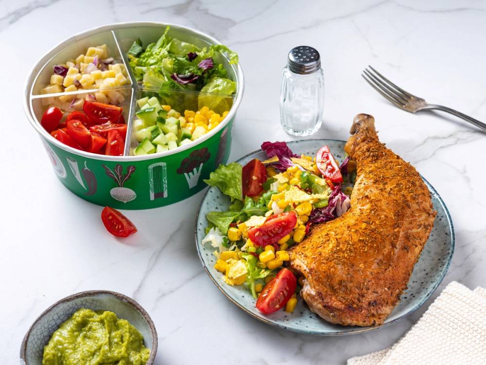 En salatbar med kyllinglår og en tallerken med salat og kyllinglår ved siden av, på et hvitt bord.