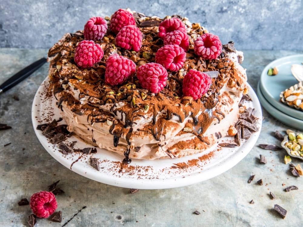 Sjokoladekake med marengsbunn pyntet med friske bringebær på toppen, ser ut til å være dekorert med sjokoladebiter og raspede sjokoladestykker.