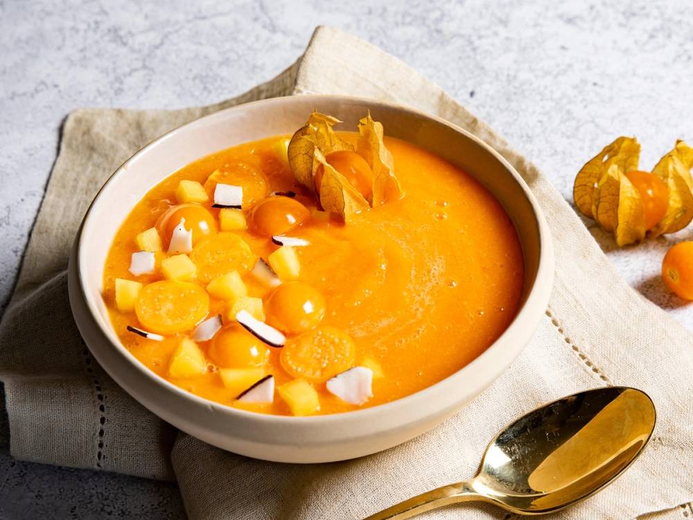 En smoothiebowl med physalis og papaya, pyntet med små terninger av frukt og kokosflak, ser fristende ut på en tallerken.