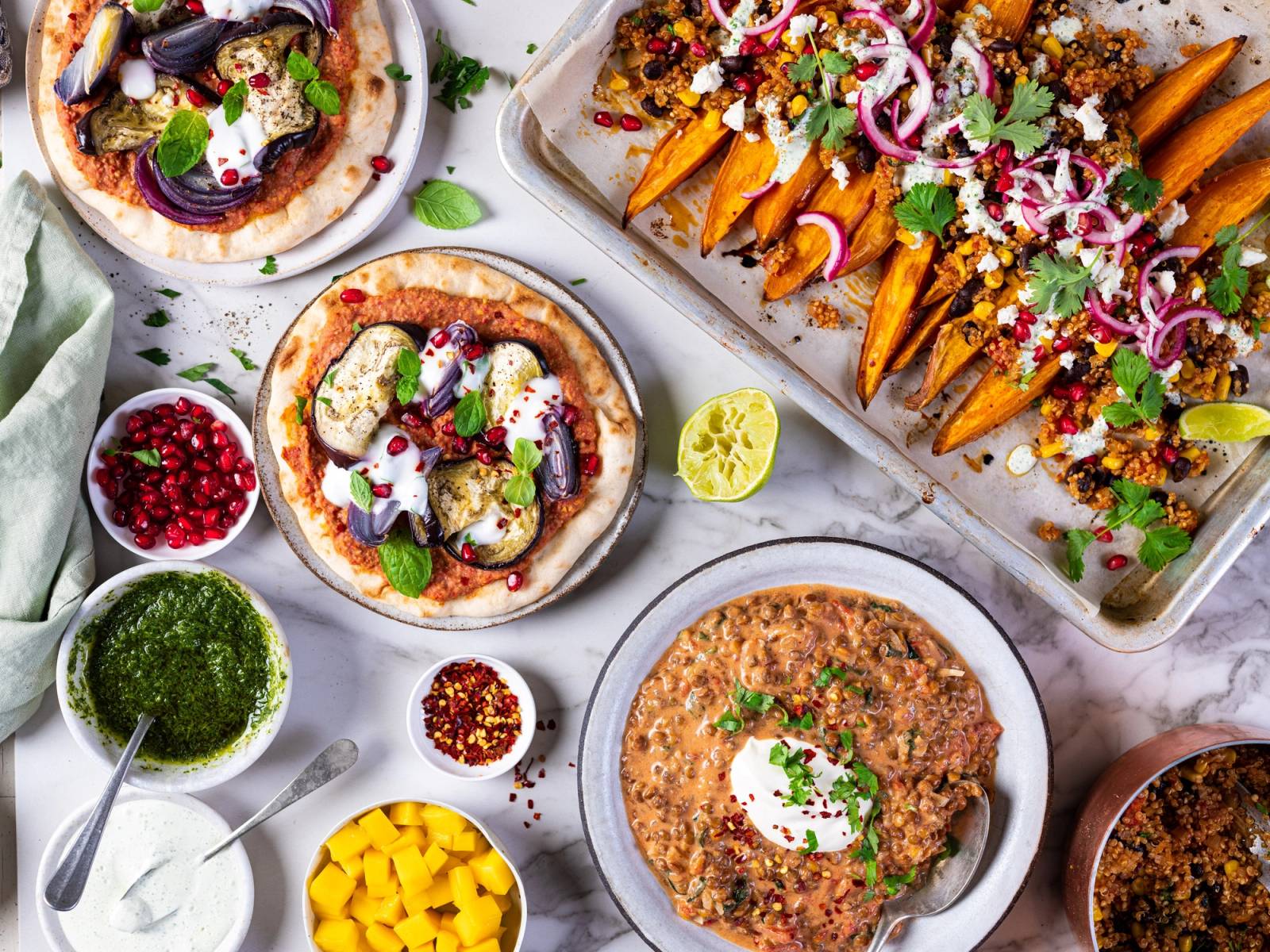 Et utvalg av meksikanske retter med tacos, guacamole, salsa og en bolle med bønner, på et hvitt bord.