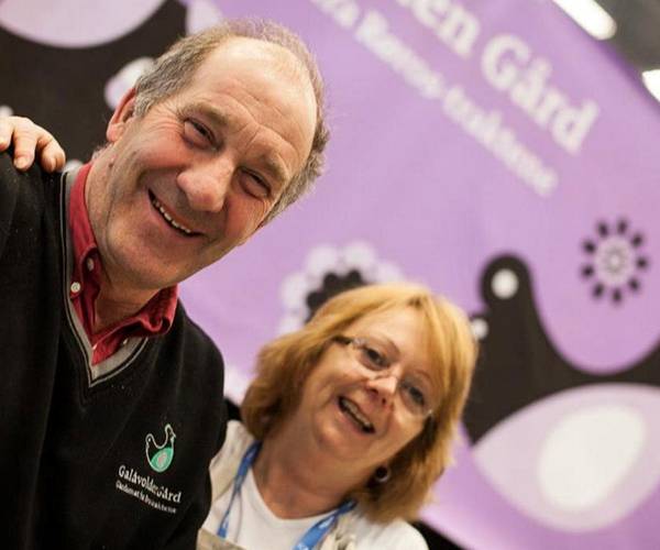 To personer står foran en vegg med en stor, lilla plakat med en and og tekst, på Ingulf_Galåvolden gård.