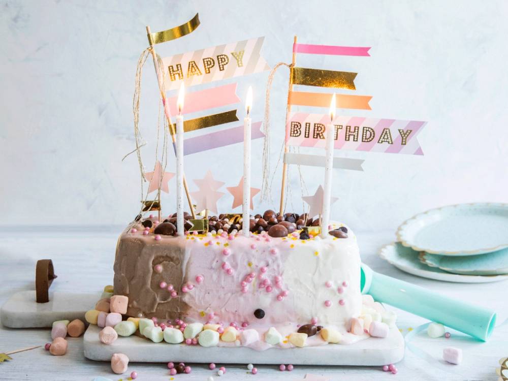 En enkel bursdagsiskake pyntet med små godterier og festpynt, med flagg og lys på toppen.
