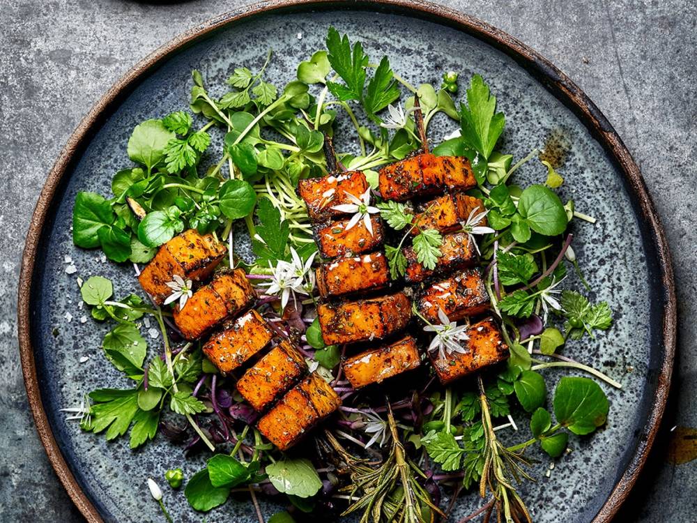 Grillet kjøtt med urter og grønne blader på en rund tallerken.