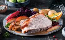 Skinkestek med ben servert på en tallerken sammen med poteter, grønnsaker og saus, omgitt av bær og sitronbåter.