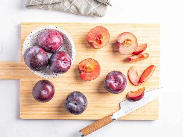 Ferske plommer på et skjærebrett med en kniv, noen er skåret opp og andre hele.