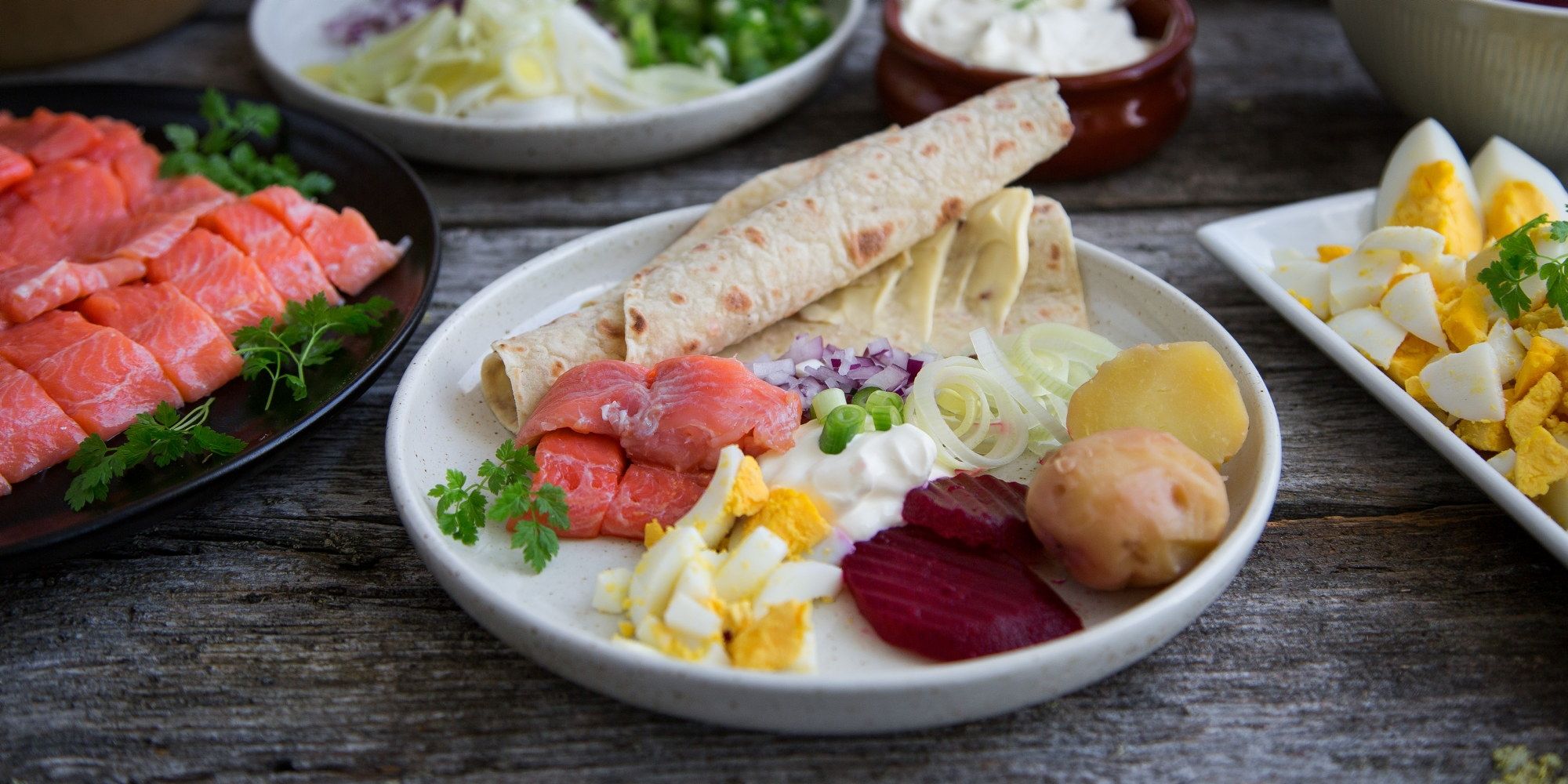 Tradisjonell rakfisk servert med tilbehør som poteter, grønnsaker og flatbrød på et fat.