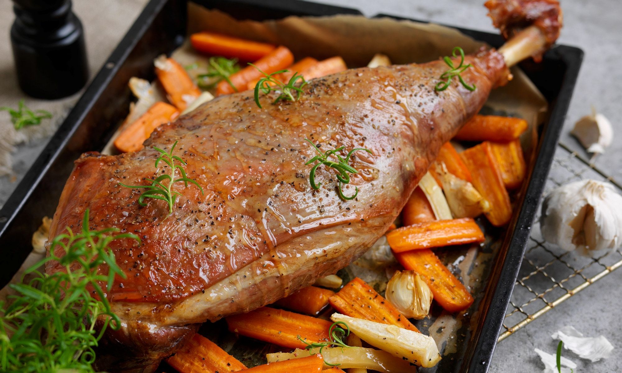 Stekt lammelår med ovnsstekte gulrøtter og selleristenger på en svart serveringsplate, pyntet med frisk grønn urter.