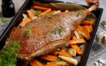 Stekt lammelår med ovnsstekte gulrøtter og selleristenger på en svart serveringsplate, pyntet med frisk grønn urter.