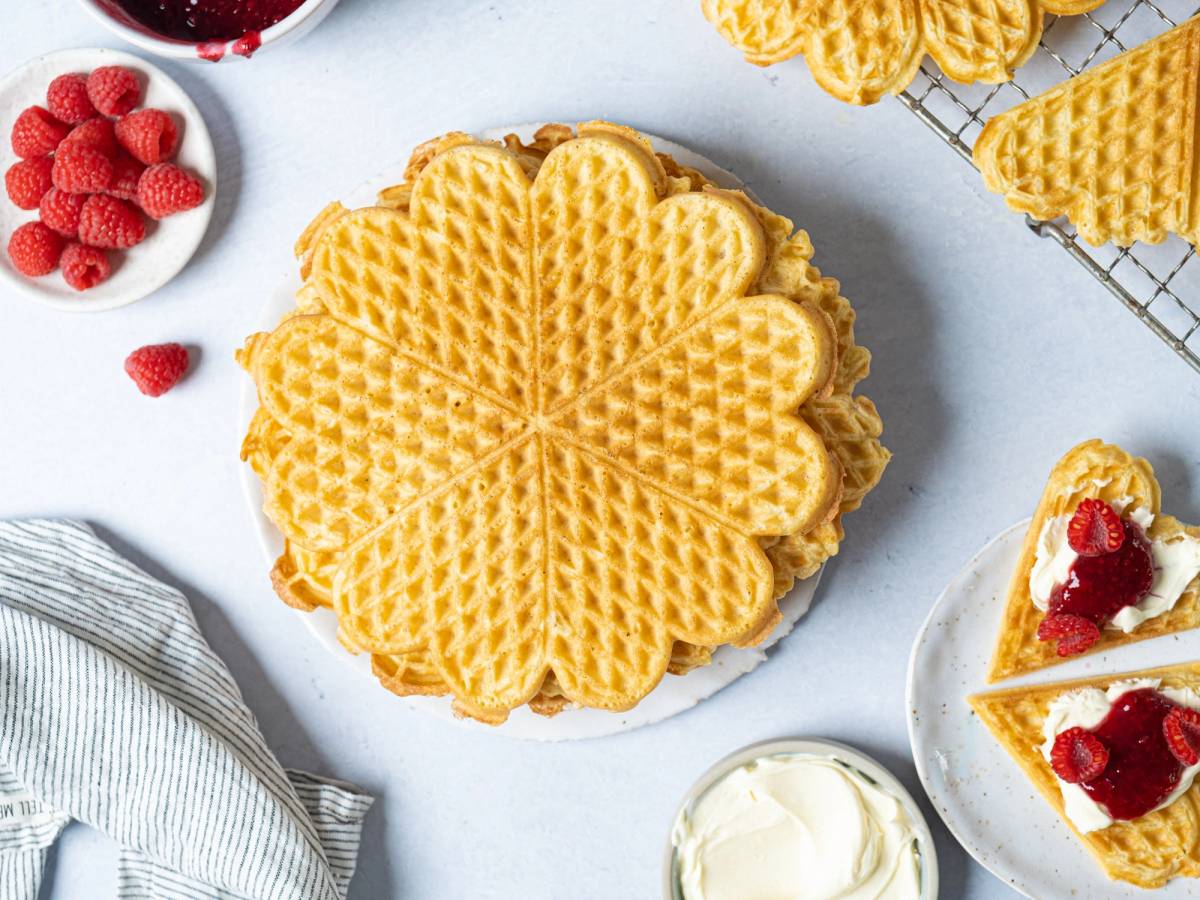 Et fat med flere varme vafler og en liten skål med bringebær på siden.