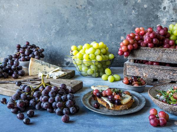 Druer i ulike farger og blåmuggost på et fat, med flere druer og ost i bakgrunnen.