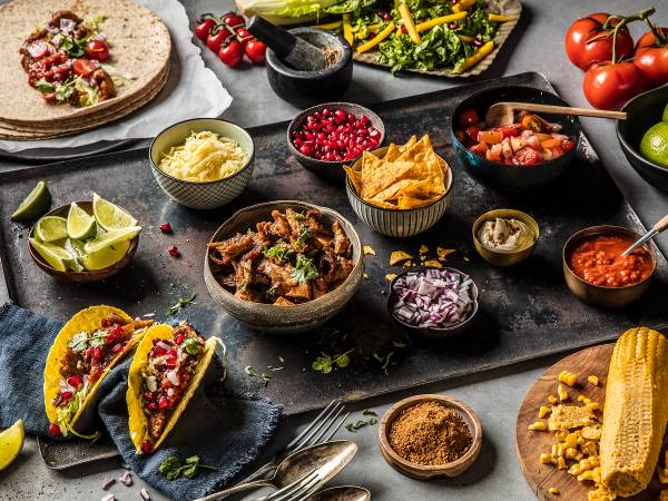 Vegetar-taco fylt med grønnsaker og serveres med limebåter og ulike tilbehør på en svart bakgrunn.