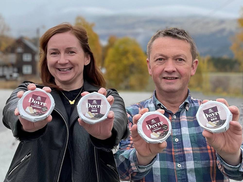 To personer holder opp små ostekartonger fra Ysteriet på Dovre, med høstfargede trær og fjell i bakgrunnen.
