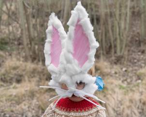 En person med påskenisse-hatt med kaninører og en påskehare-maske med store øyne, utendørs i naturen.