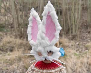 En person med påskenisse-hatt med kaninører og en påskehare-maske med store øyne, utendørs i naturen.