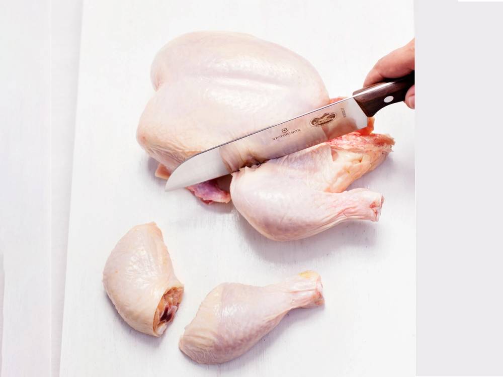 En person skjærer opp en rå kylling på et skjærebrett med en kniv.