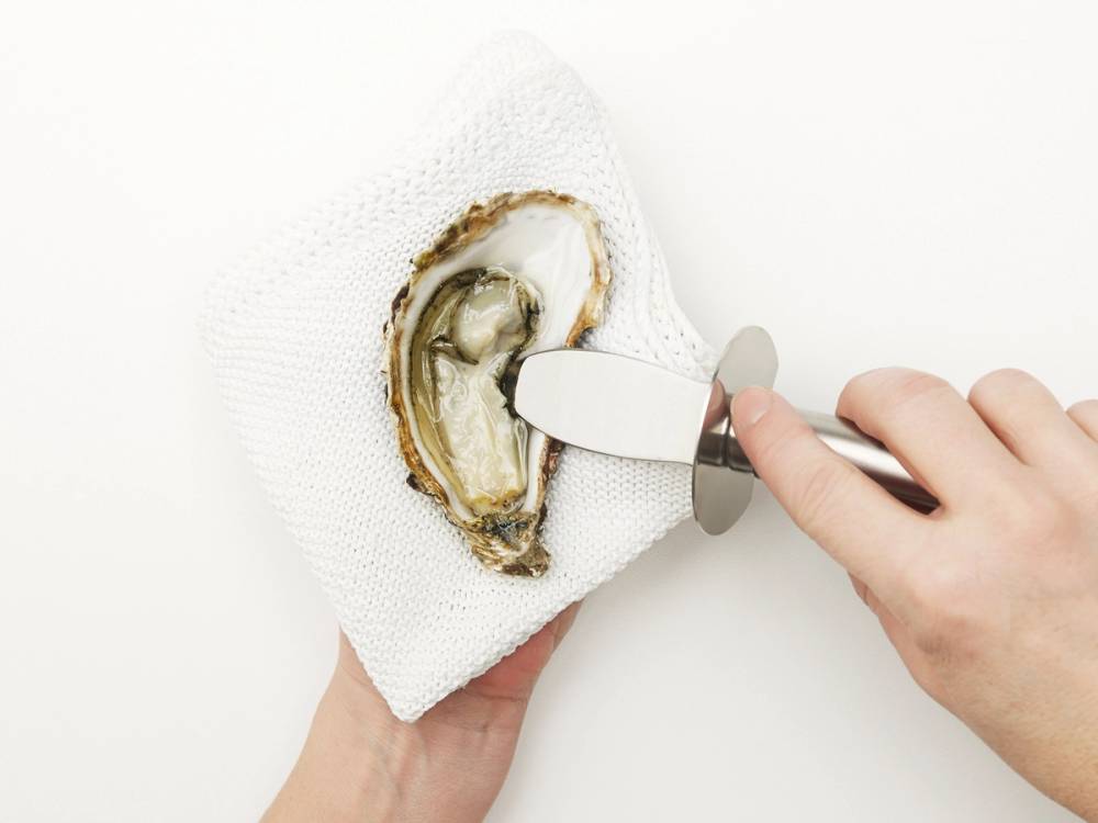 En person bruker en skje for å åpne en østers på en hvit bakgrunn.