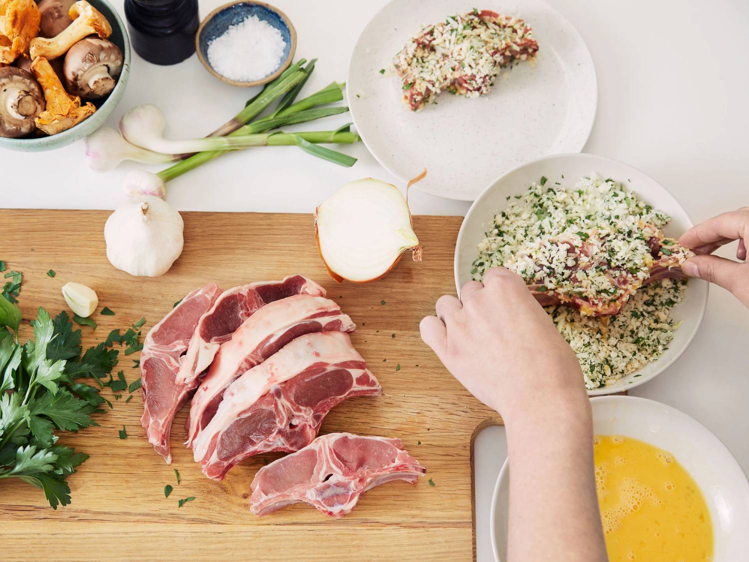 Hånd som legger fylt paprika i en bolle med ris og urter, omgitt av rått kjøtt, grønnsaker og krydder på kjøkkenbenken.