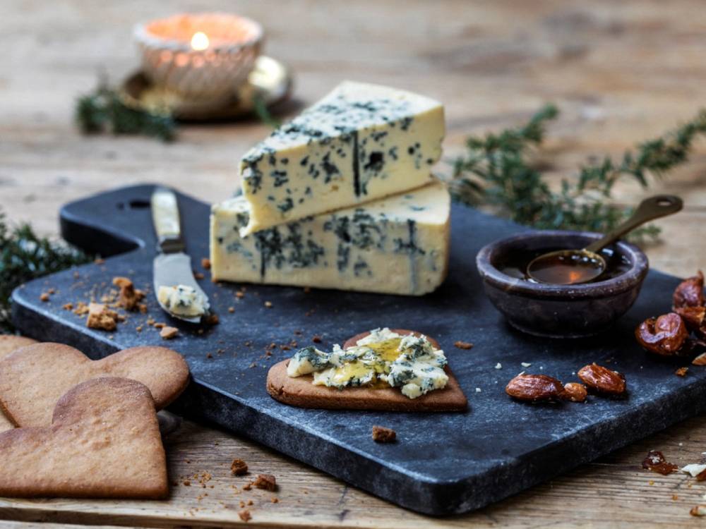 Blåmuggost på en skjærefjøl med kjeks og honning, med et lys i bakgrunnen, på et treverk.