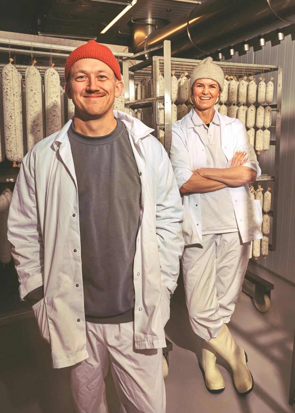 To personer i arbeidsklær står i en butikk med hyller fylt med garn eller tråd i bakgrunnen.