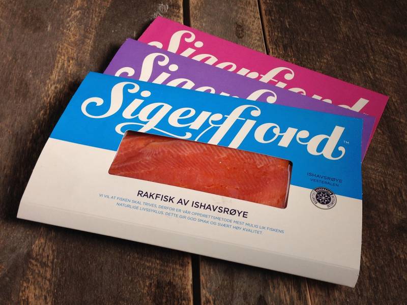 Pakke med Sigerfjord-merkede lakseprodukter på en treoverflate, med tydelig Sigerfjord-logo og tekst om råfisk av ishavsrøye.