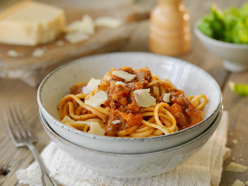Linguini med bolognesesaus og revet parmesanost på en tallerken.