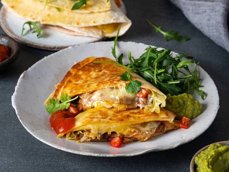 En tortilla wrap fylt med ost, grønnsaker og kjøtt, ser ut til å være delt i to på en hvit tallerken med salat ved siden av.