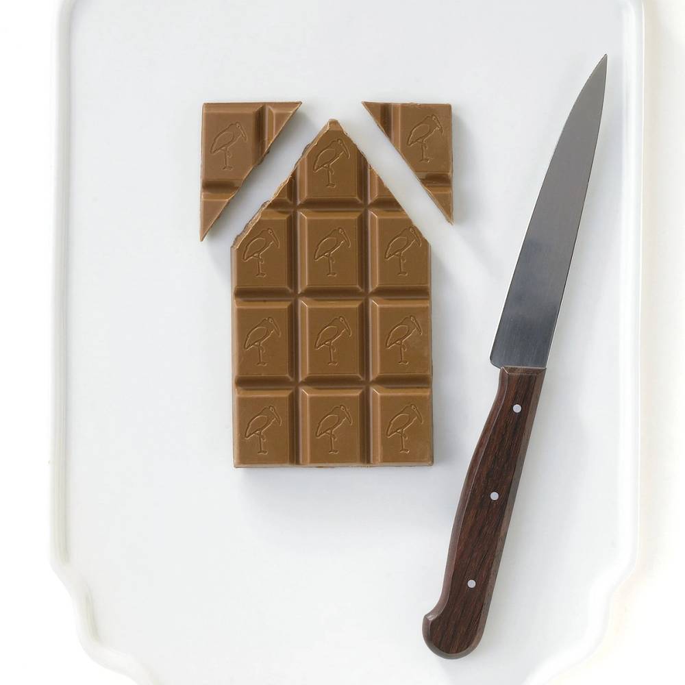 Et sjokoladehus under bygging med en kniv ved siden av, deler av sjokoladen er kuttet ut i kvadratiske former.
