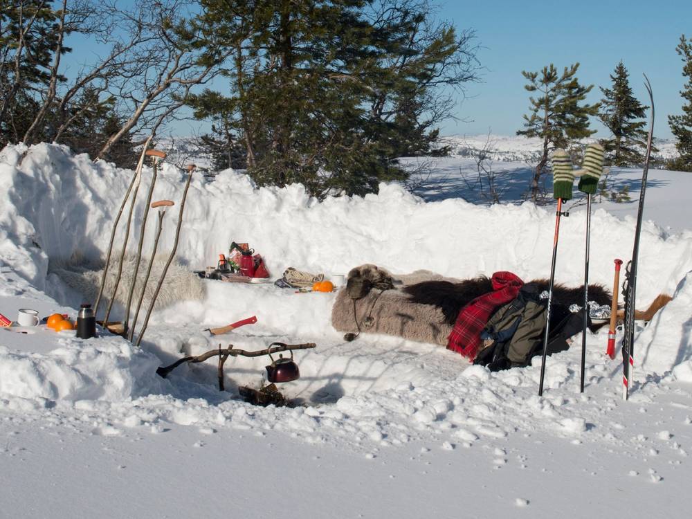 En person ligger i snøen med utstyr til skikjøring eller snøaktiviteter rundt seg i et vinterlandskap.