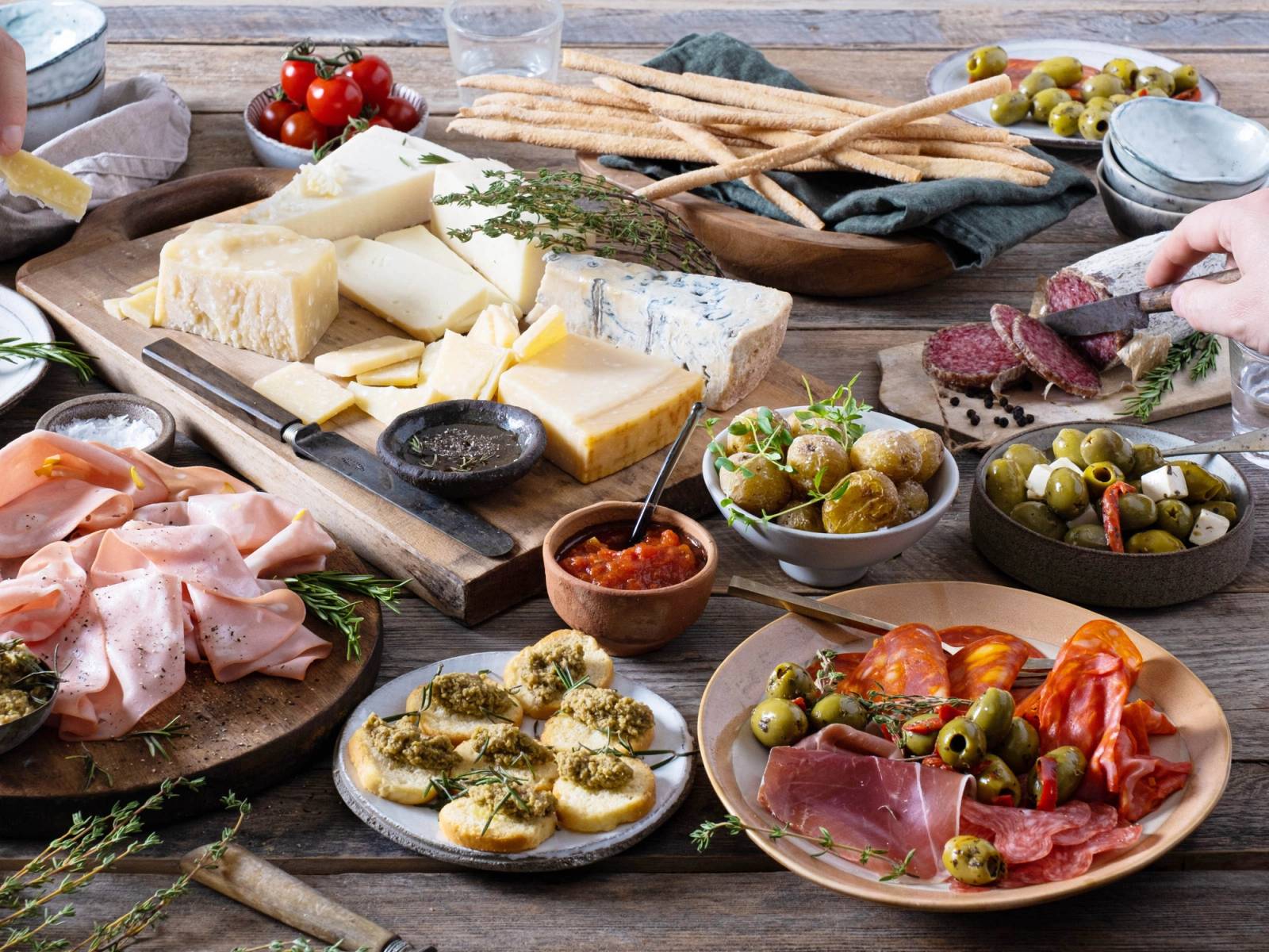 Et utvalg av tapas med ost, skinke, oliven, brød og grønnsaker på et bord.