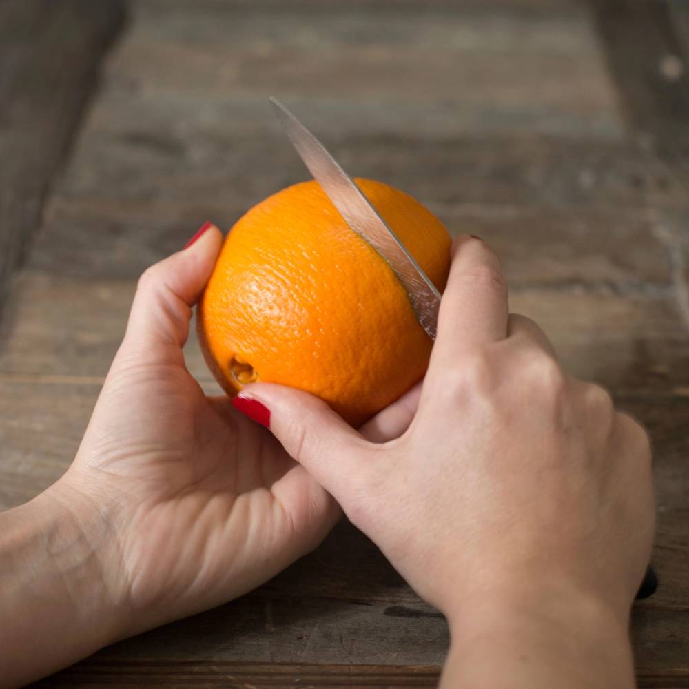 Person som skreller en klementin med en kniv på et trestykke bord