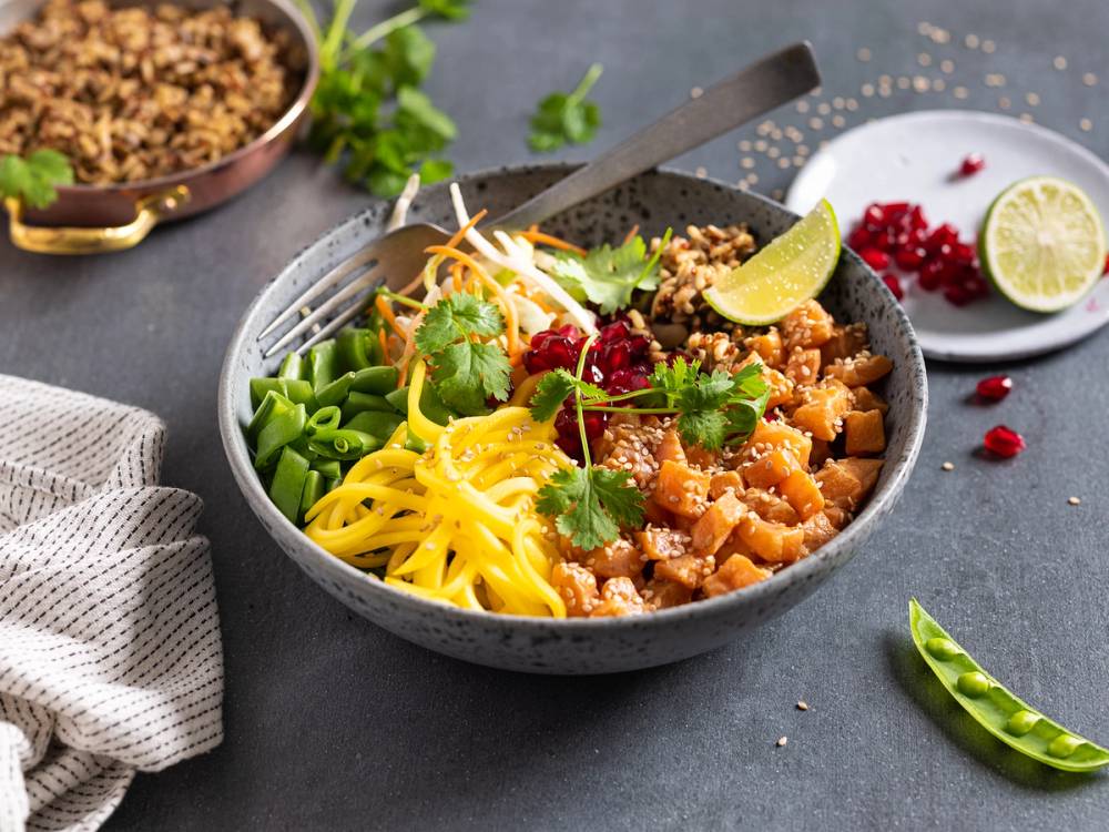 En pokésalat med laks, grønnsaker, sitron og nudler i en bolle på et bord