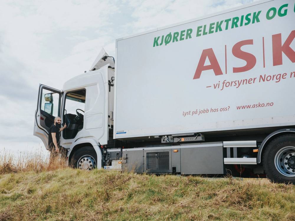 ASKO-lastebil parkert på en åpen mark med gress og åker i bakgrunnen.