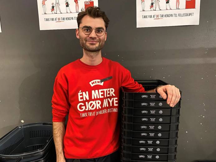 En person i rød genser står ved en hylle med handlekurver laget av havplast, uten å vise ansiktet tydelig.