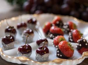 Nyttårsbordet med små kaker og fruktdekorasjoner, blant annet jordbær og kirsebær, pyntet med sølvkuler og sjokoladetrekk.