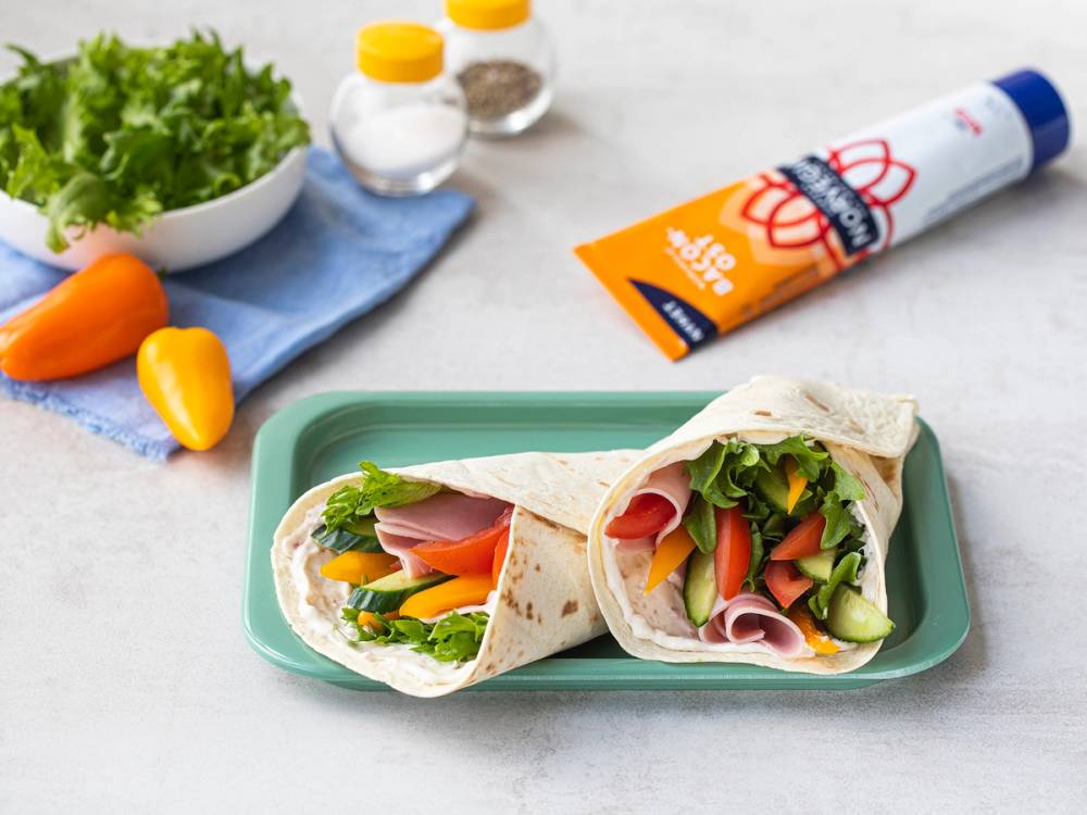 Wraps fylt med smøreost, skinke og grønnsaker på en grønn tallerken, med salat og krydder på siden.