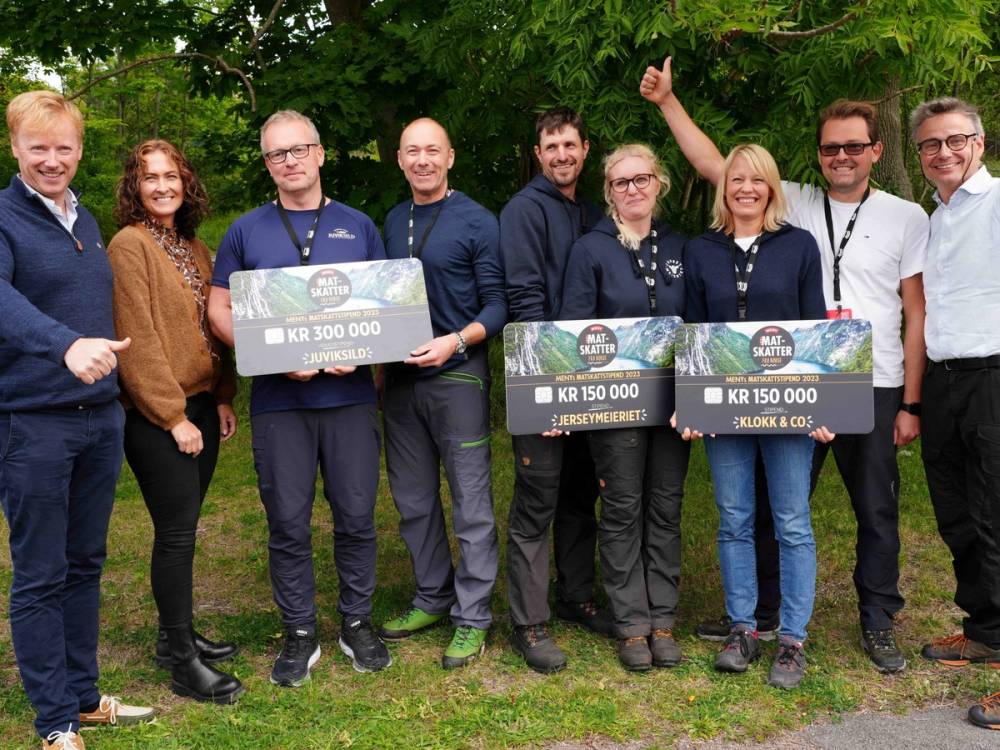 Vinnerne av Matskattstipendiet MENY 2023 står sammen utendørs med store sjekker, omgitt av grønne trær.