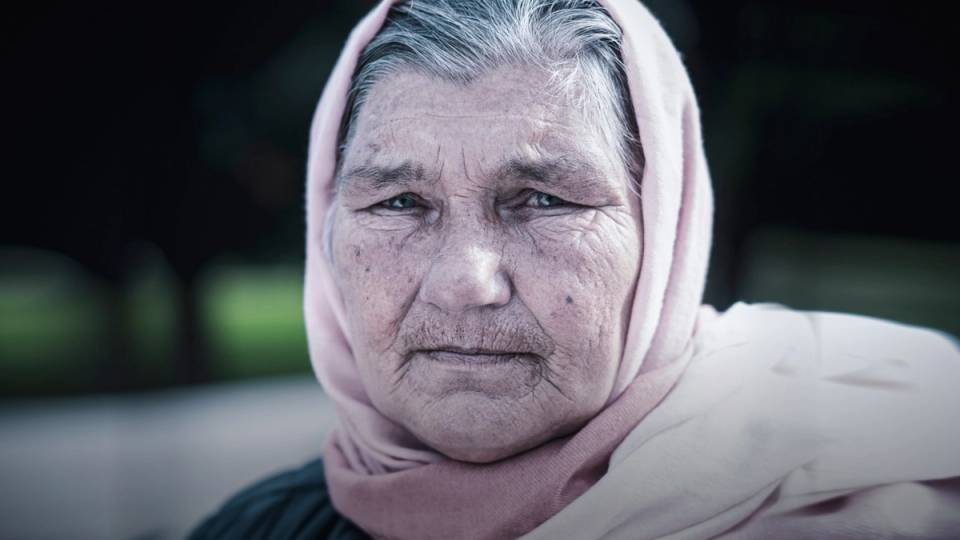 Person med hettegenser og ansikt dekket av en hvit papirpose, ute i naturen.