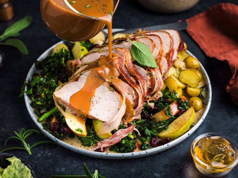 Baconstekt kalkunfilet på en tallerken med grønnsaker og poteter, med saus som helles over kjøttet.