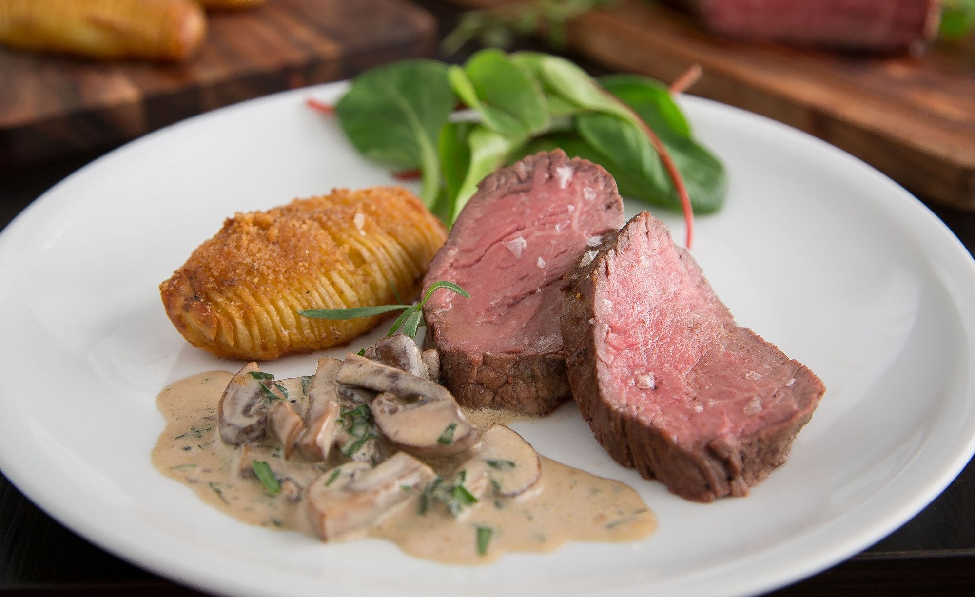 Indrefilet av okse servert med soppstuing og grønne blader på en hvit tallerken.