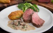 Indrefilet av okse servert med soppstuing og grønne blader på en hvit tallerken.