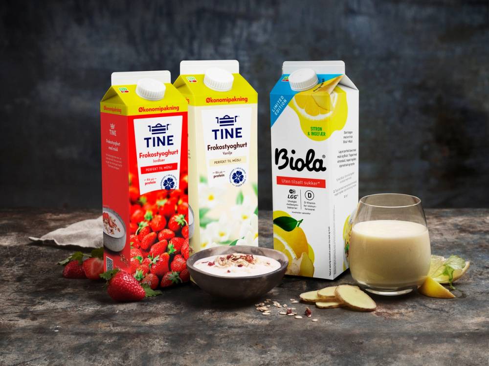Tre melkekartonger av TINE og Biola-yoghurt med frukt og en glass melk på et bord.