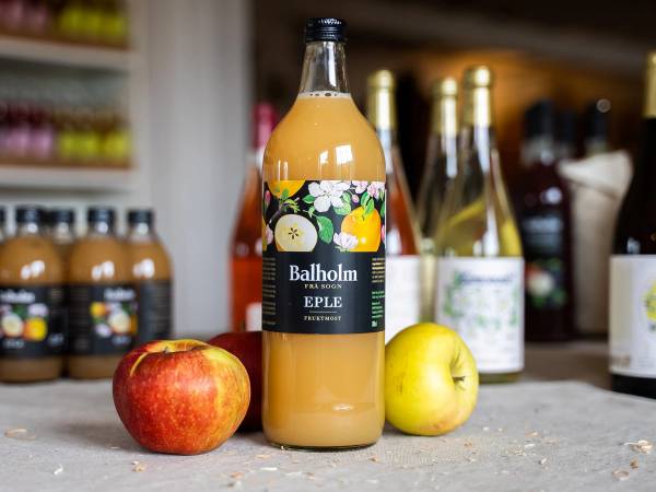 En flaske eplejuice står på en kjøkkenbenk sammen med en rød og en gul eple, med andre flasker i bakgrunnen.