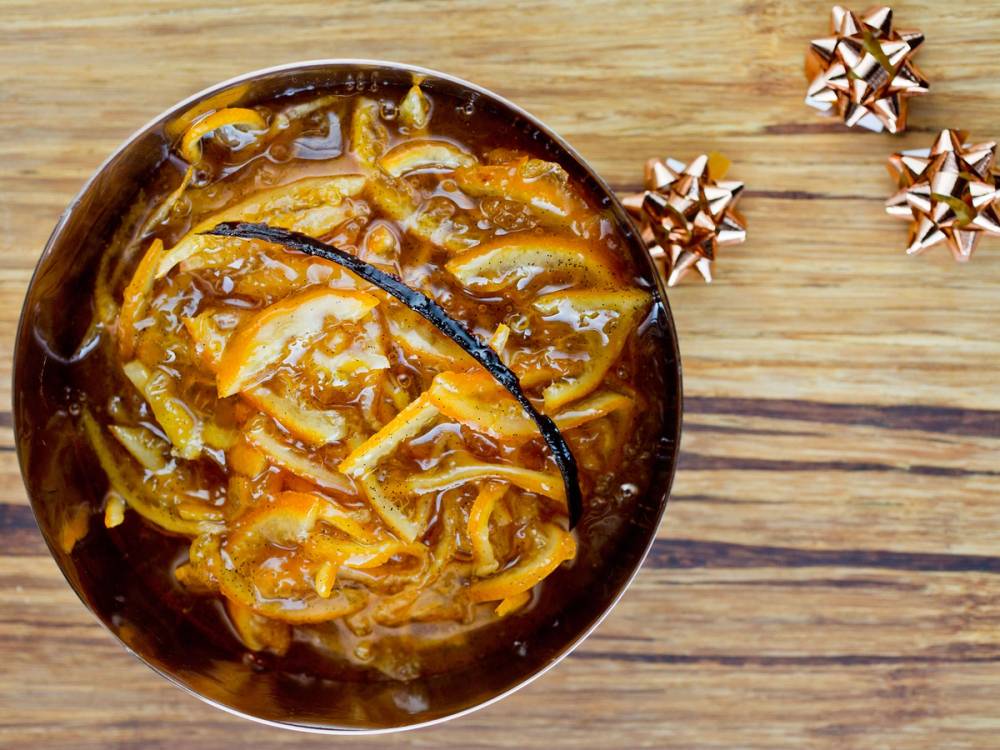 Klar til julens klementinmarmelade i en skål med skiver av klementin og karamellisert sukker, omgitt av små julegaver på et trebord.