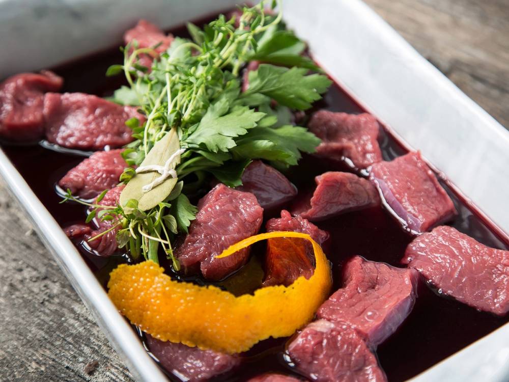 Biter av biff i rødvinssaus med sitrus og urter som pynt, servert i en hvit serveringsskål.