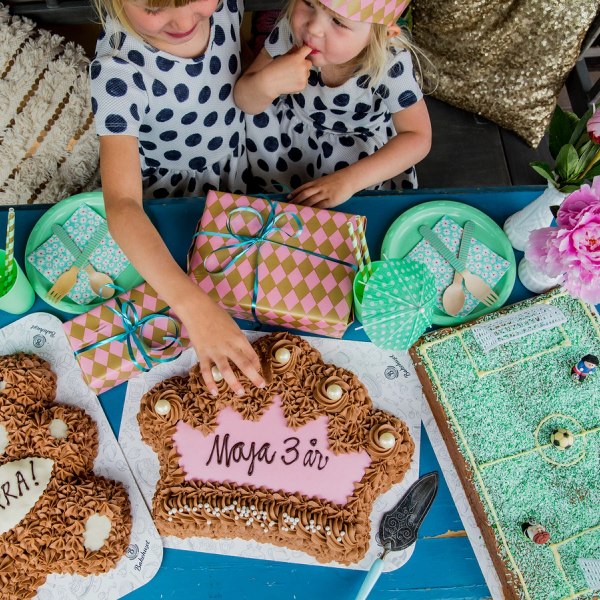 Barn som feirer bursdag med kaker og gaver på et bord, pyntet med blomster og borddekking.