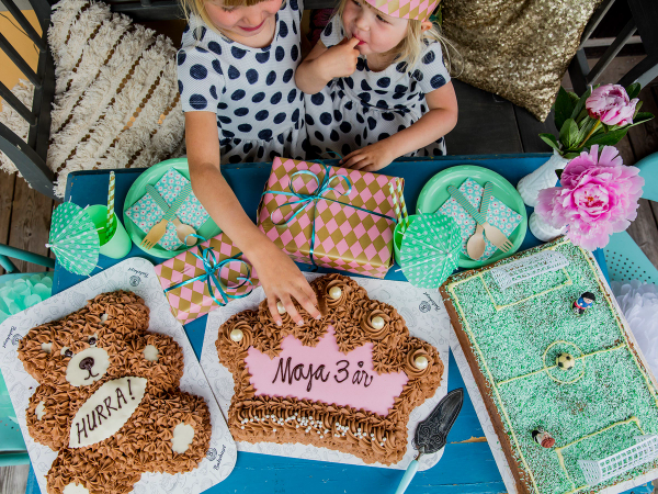 Barn som feirer bursdag med kaker og gaver på et bord, pyntet med blomster og borddekking.